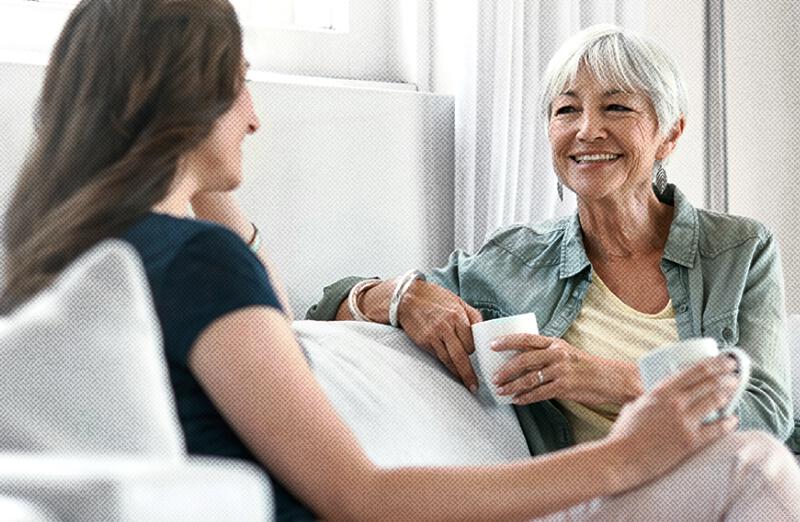 A PureWick&trade; System caregiver and her mother sit on a couch drinking coffee